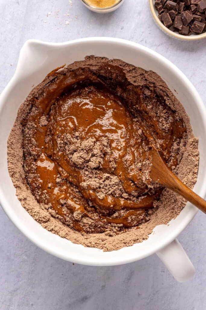 Stirring with a wooden spoon the dry and wet ingredients to form the pumpkin spice chocolate loaf batter.