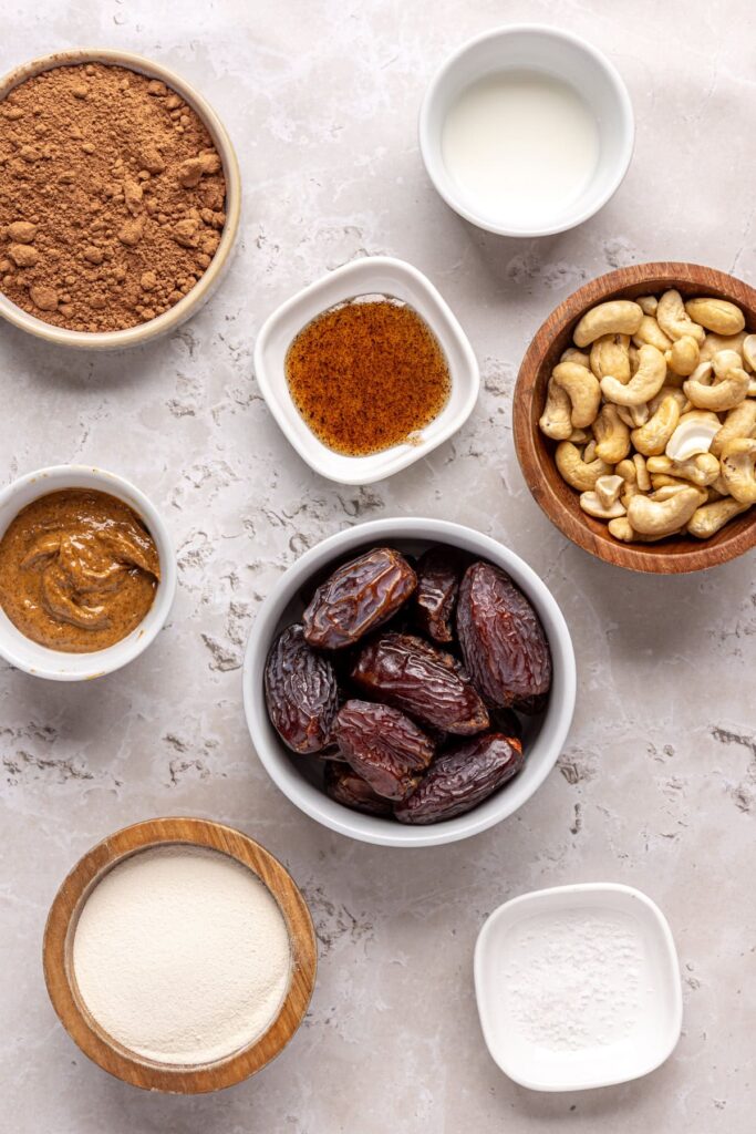 Overhead shot of ingredients for protein brownie bites, including dates, cashews, cacao, collagen peptides, and almond butter