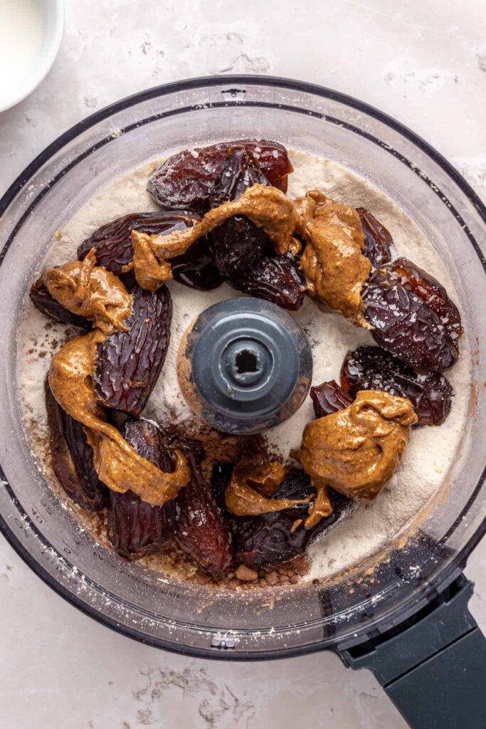 Food processor filled with dates, cacao powder, collagen, almond butter, and vanilla for brownie bite dough