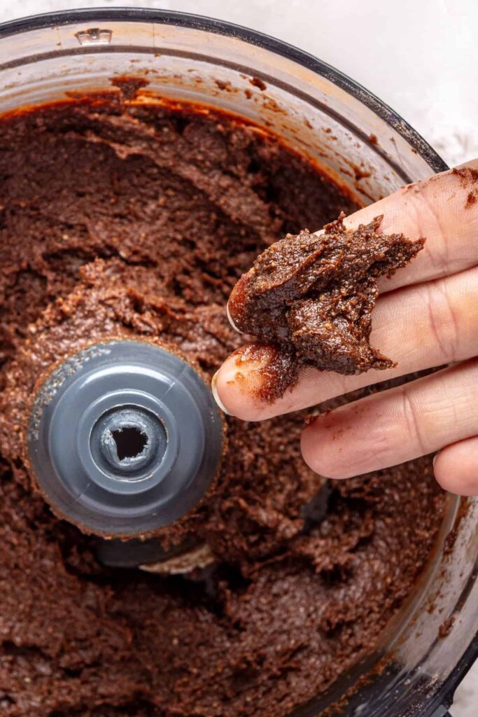 close-up of a hand holding the brownie bite mixture that's been blended into a sticky dough before rolling into balls