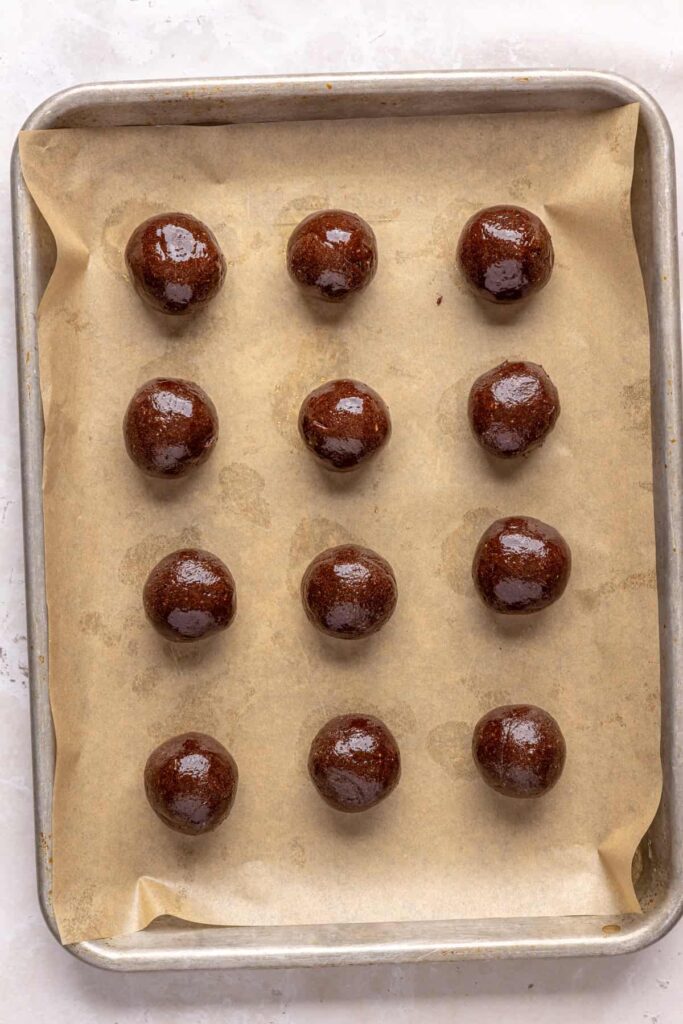protein brownie mixture rolled into small no-bake balls on a parchment paper-lined baking sheet