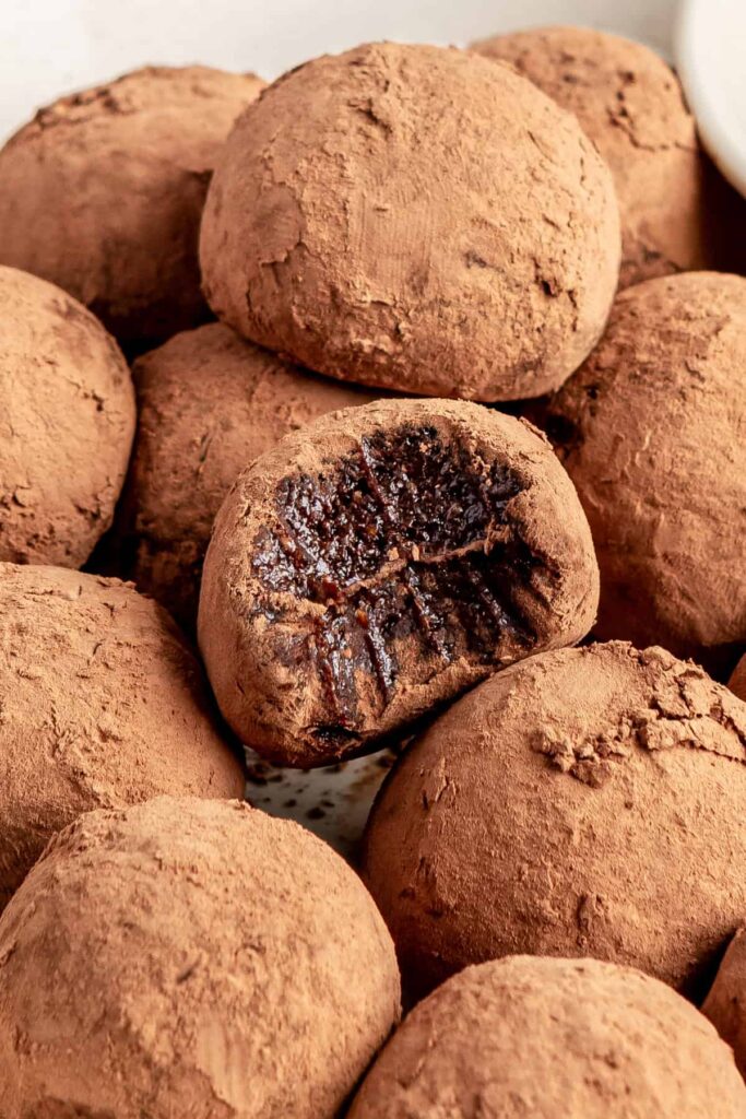 close-up of a protein brownie bite with a bite taken out, showing fudgy chocolate interior, with other protein balls on a plate