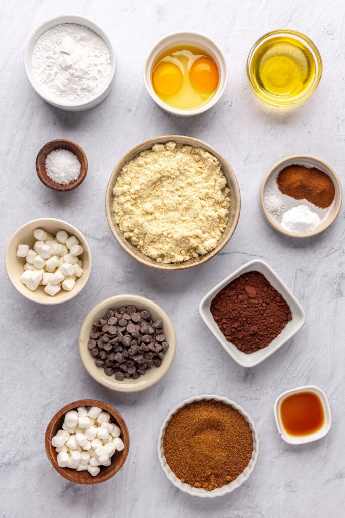 Overhead shot of ingredients for hot cocoa cookies, including almond flour, cocoa powder, chocolate chips, and mini marshmallows