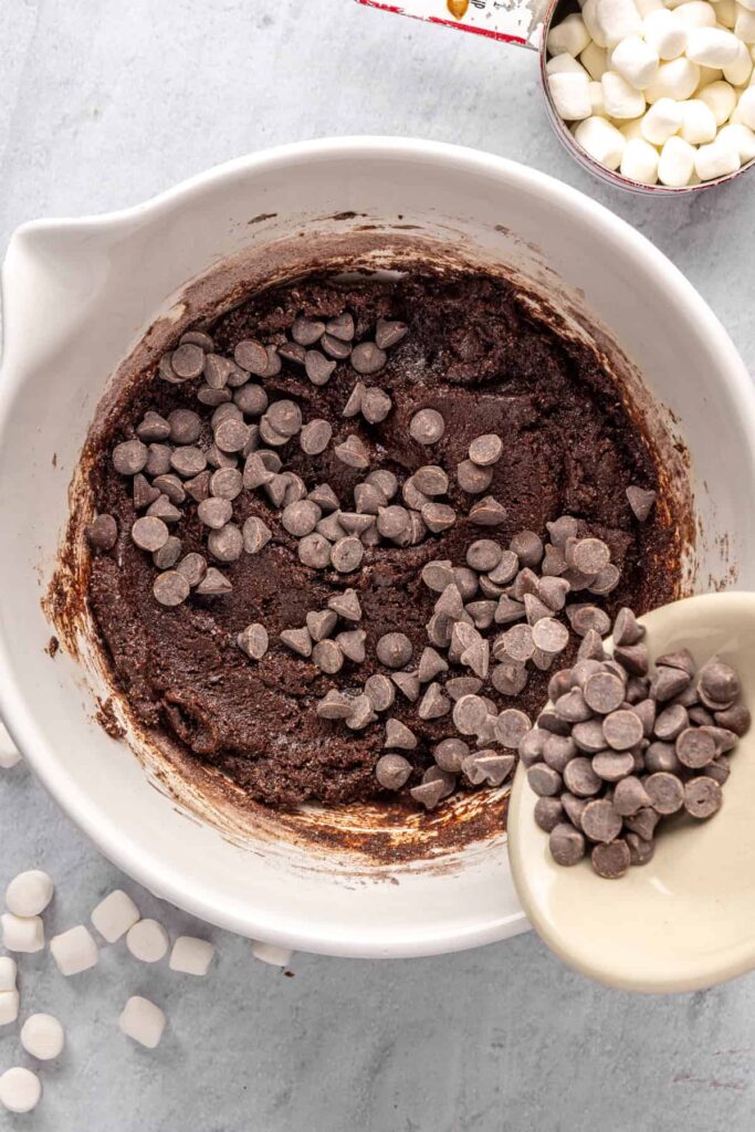pouring chocolate chips into hot cocoa cookie dough