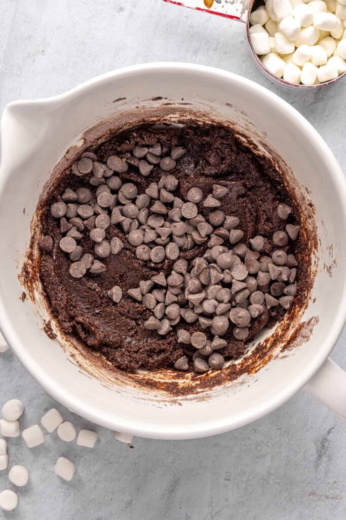 chocolate chips in a large mixing bowl on top of hot cocoa cookie dough, ready to be folded in