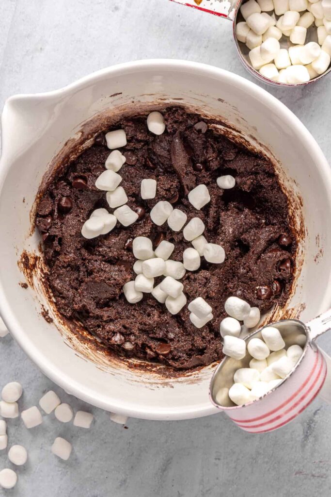 pouring mini marshmallows into hot cocoa cookie dough