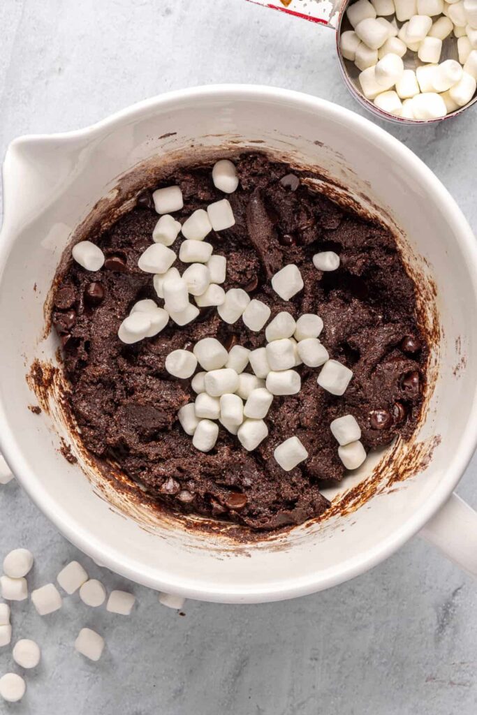 mini marshmallows in a large mixing bowl on top of hot cocoa cookie dough, ready to be folded in