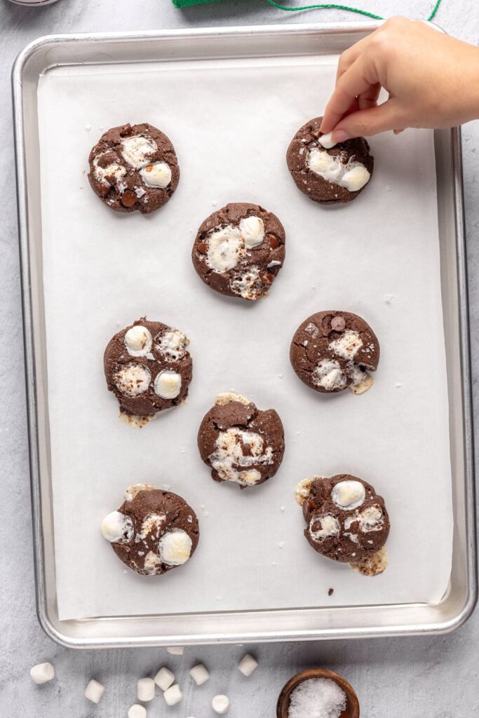 Adding mini marshmallows to the top of hot cocoa cookies after baking