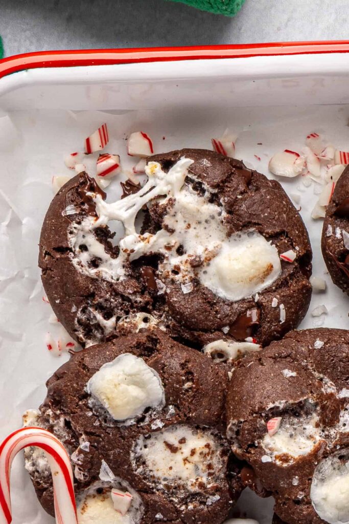 close-up of a fresh hot cocoa cookie torn in half with melty, gooey marshmallows, arranged with candy canes on a festive tray