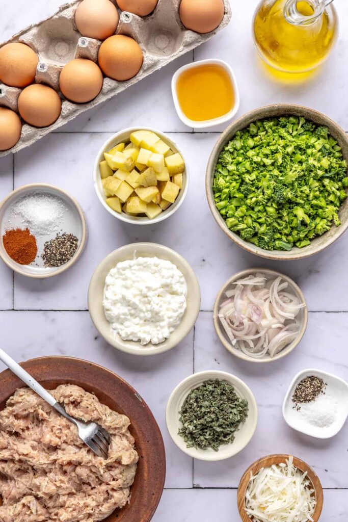 Overhead shot of ingredients for Chicken & Veggie Egg Bake including eggs, potatoes, broccolini, sage, and sausage