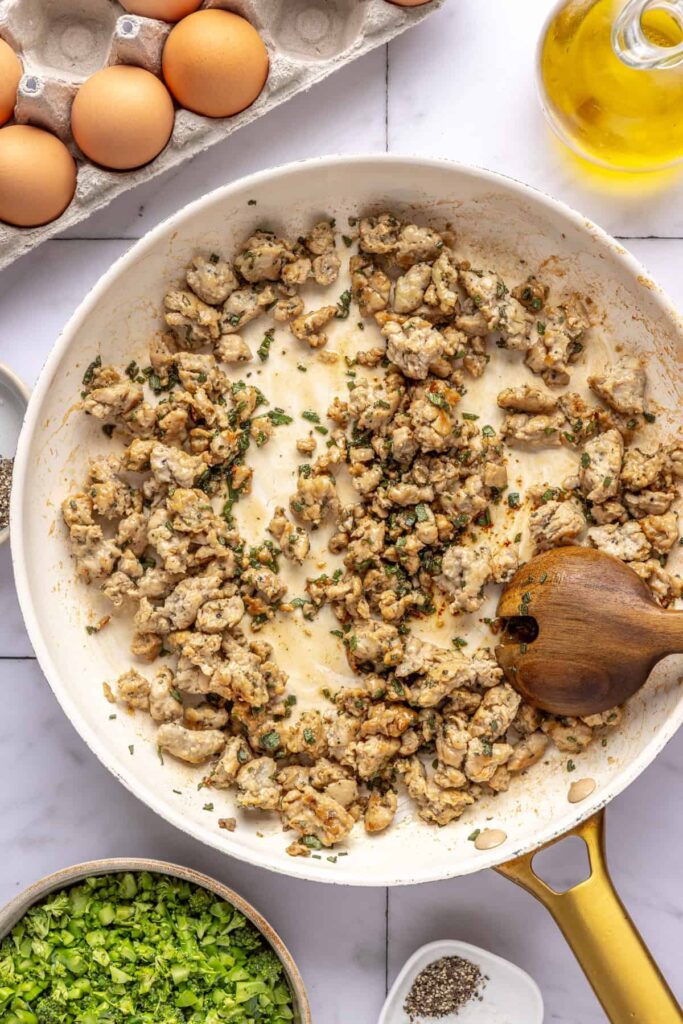stirring Golden, crispy maple sage chicken sausage in skillet for egg bake