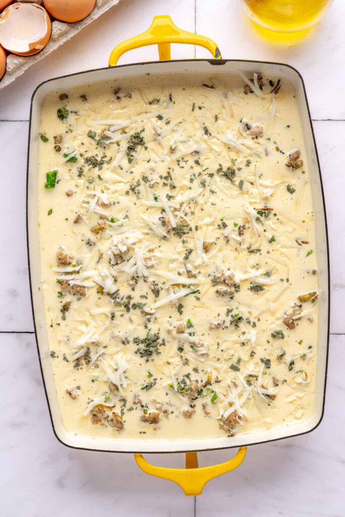 Unbaked Chicken & Veggie Egg Bake topped with goat cheddar and sage in a 9x13 pan before baking