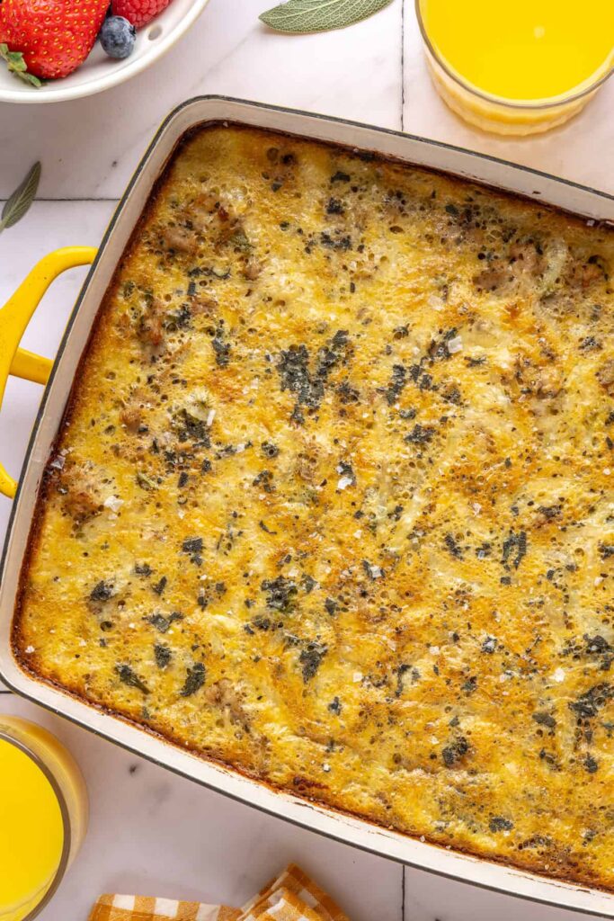 Baked Chicken & Veggie Egg Bake with maple sage chicken and veggies in a 9x13 dish, styled on a table with glasses of orange juice, berries and plates