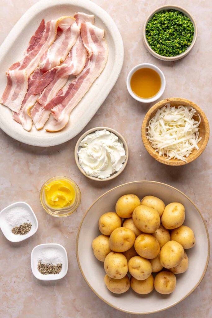 Ingredients for twice baked potatoes including mini Dutch potatoes, goat cheese, ghee, chives, shredded cheddar, chicken stock, and no-sugar-added bacon