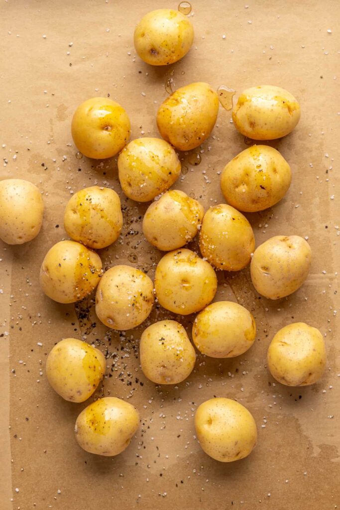 Mini Dutch potatoes coated in bacon grease and seasoning on a baking sheet