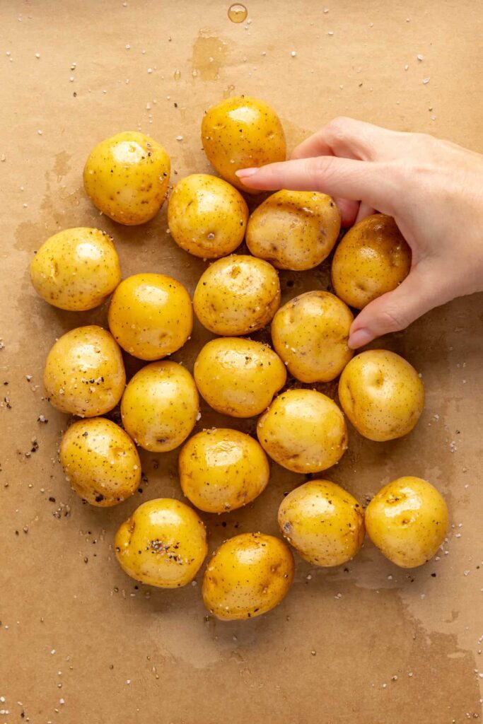massaging the bacon grease and seasoning on the mini Dutch potatoes on a parchment paper-lined baking sheet, before placing in the oven