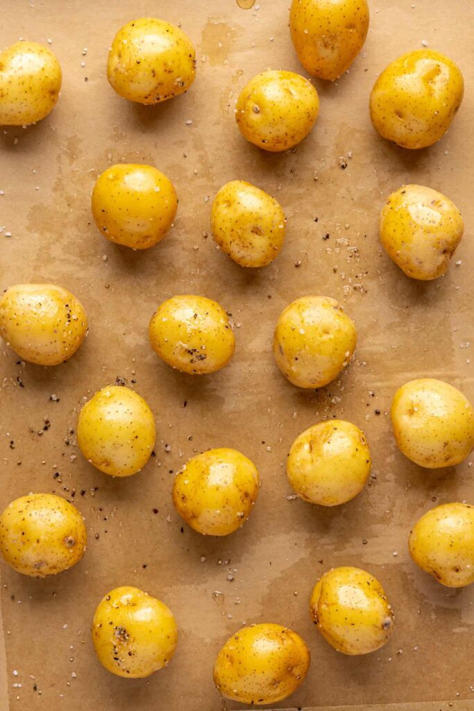 Mini Dutch potatoes coated in bacon grease and seasoning on a baking sheet
