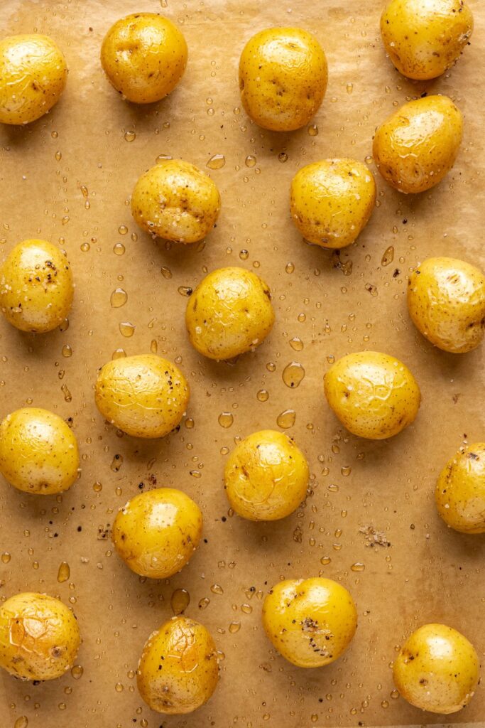 Mini Dutch potatoes coated in bacon grease and seasoning on a baking sheet