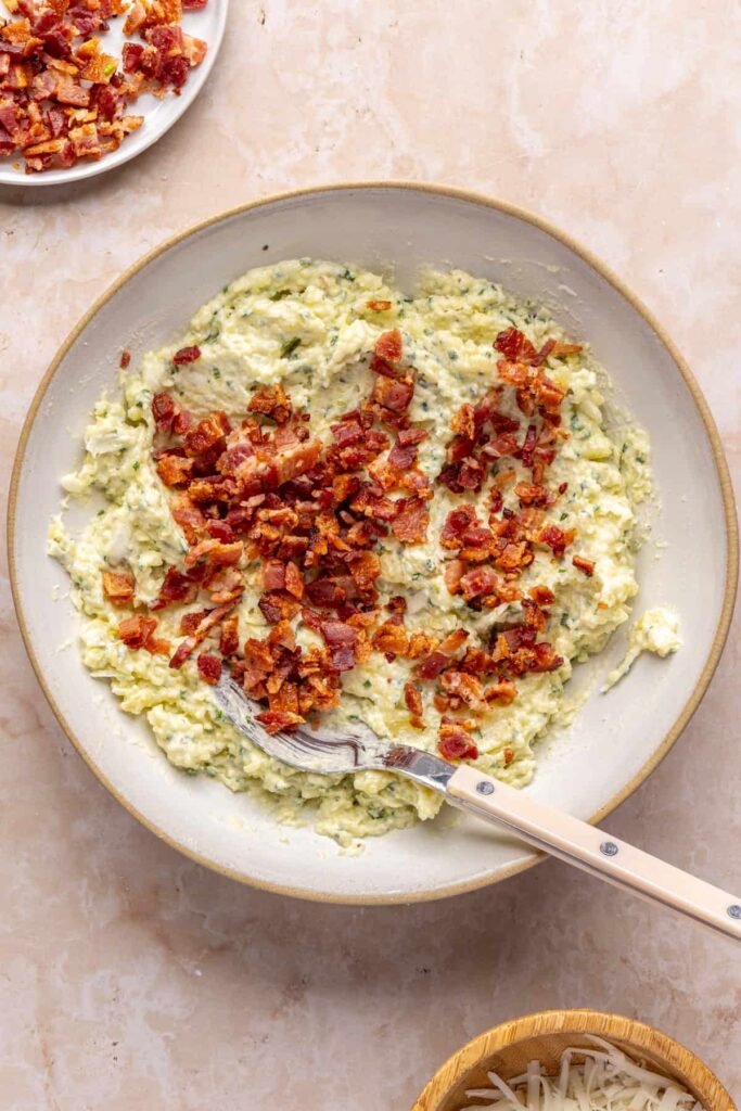 Smooth potato filling with bacon bits on top, ready to be mixed in to complete the filling