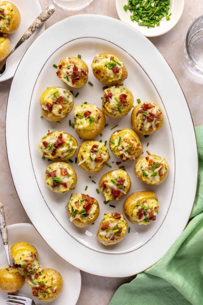 Overhead view of creamy twice baked potatoes on a white serving tray, garnished with chives and bacon