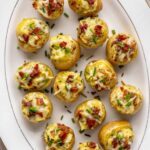 Overhead view of creamy twice baked potatoes on a white serving tray, garnished with chives and bacon