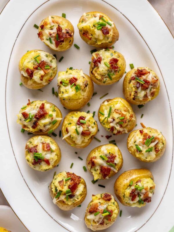 Overhead view of creamy twice baked potatoes on a white serving tray, garnished with chives and bacon