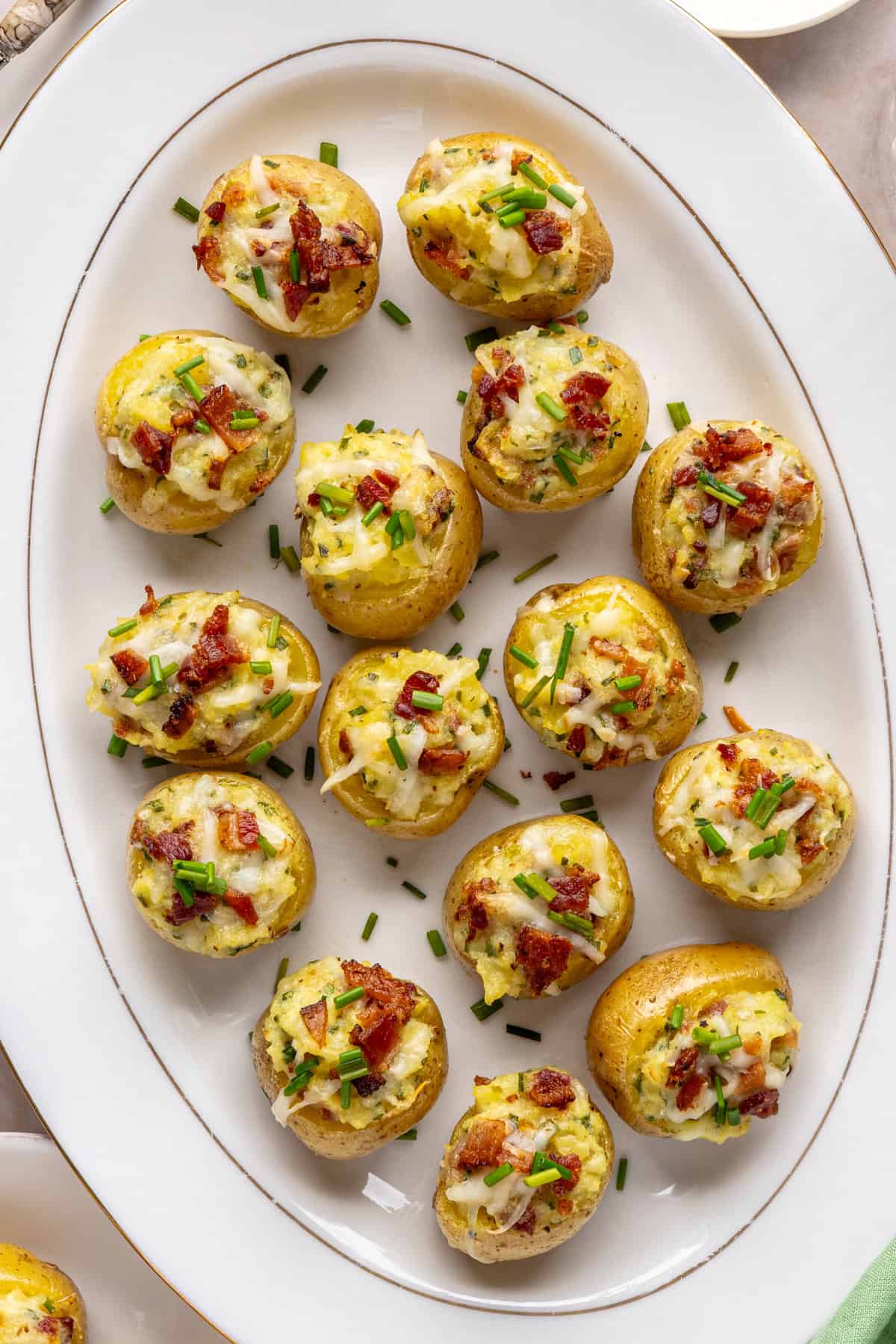 Overhead view of creamy twice baked potatoes on a white serving tray, garnished with chives and bacon