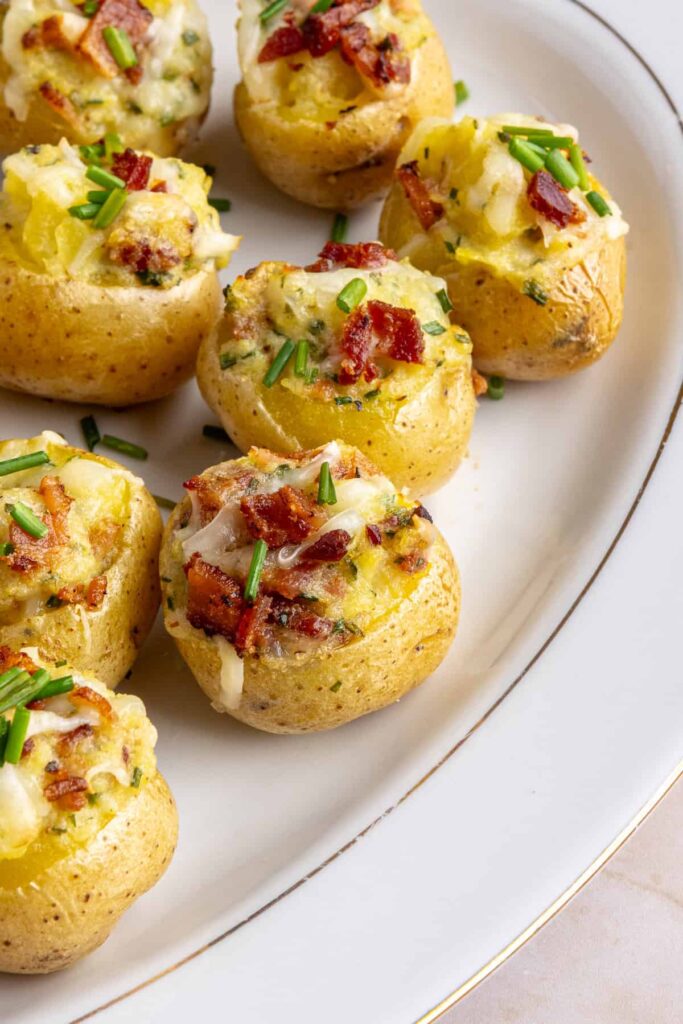 “Angled view of creamy twice baked potatoes topped with bacon and chives on a serving plate