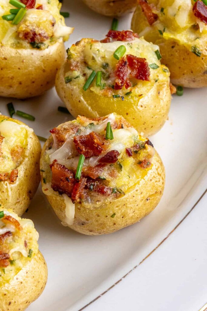 “Angled view of creamy twice baked potatoes topped with bacon and chives on a serving plate