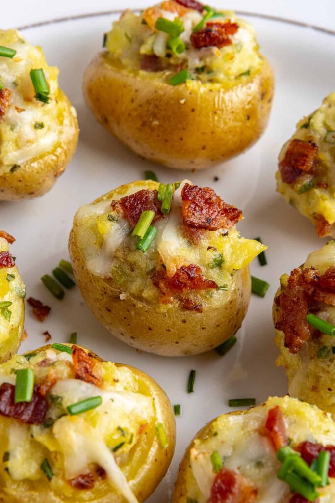 “Angled view of creamy twice baked potatoes topped with bacon and chives on a serving plate