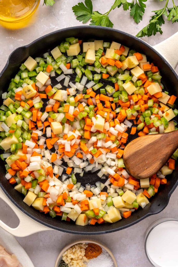 Diced celery, carrots, potatoes, and onion sautéing in a skillet for chicken pot pie