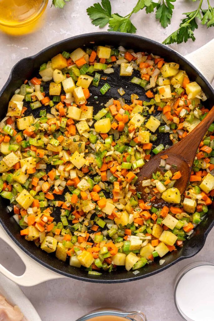 Diced celery, carrots, potatoes, and onion sautéing in a skillet for chicken pot pie
