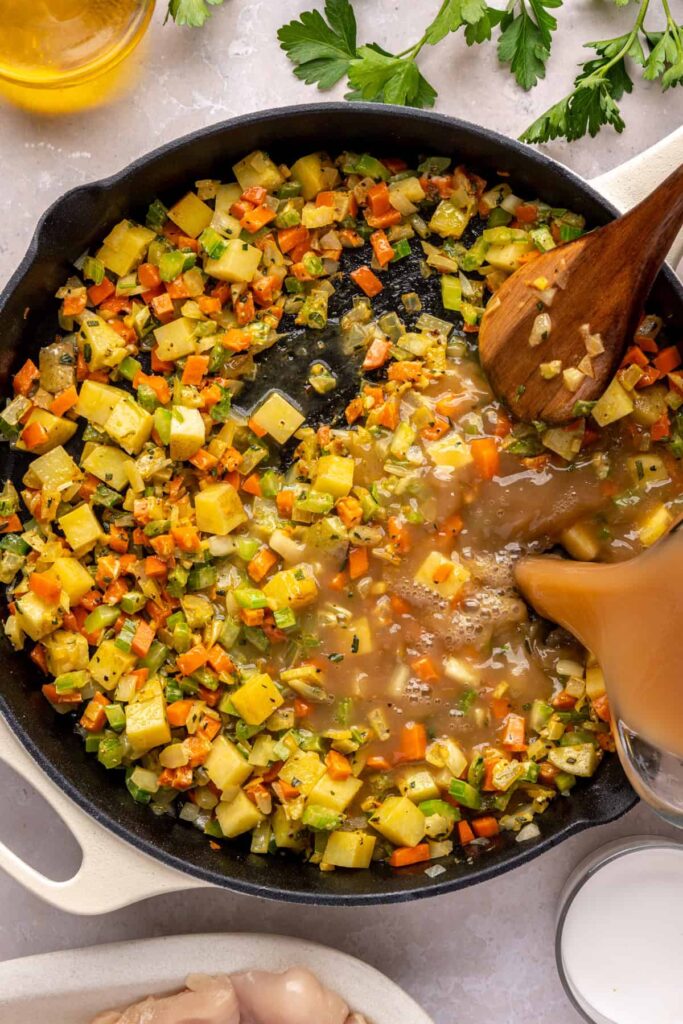 Bone broth and being poured into skillet to create creamy chicken pot pie sauce.