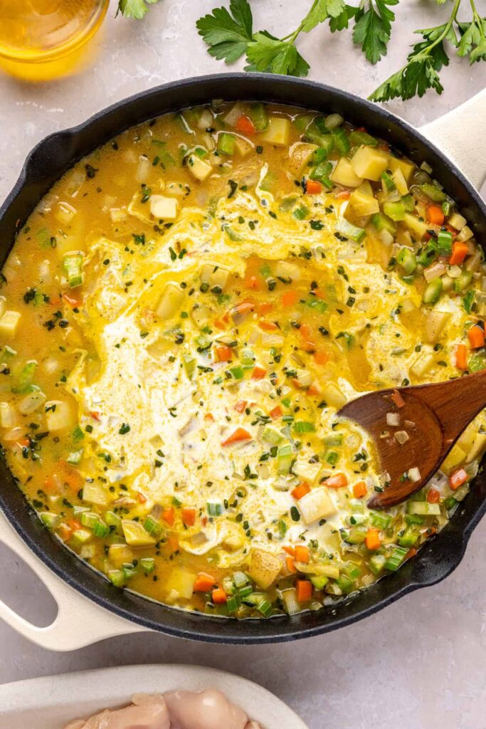 stirring bone broth and coconut milk in a skillet to create creamy chicken pot pie sauce.