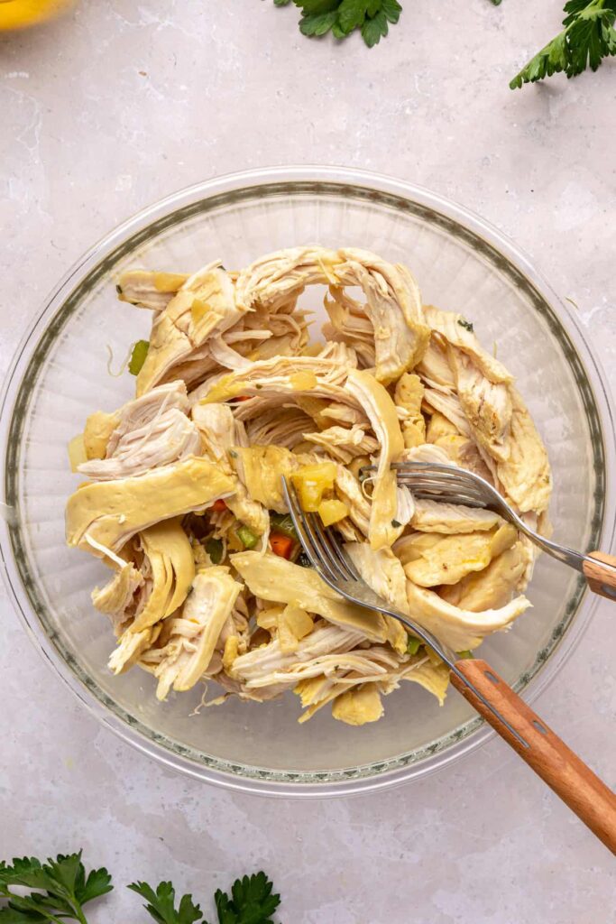 Cooked chicken breasts being shredded on a cutting board with two forks.
