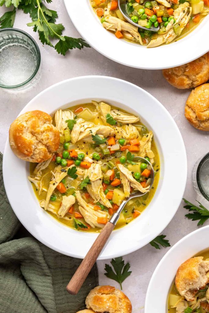 Cozy one pot chicken pot pie in bowls with biscuits for dipping, styled on a table with napkins and a glass of water, photographed from above,