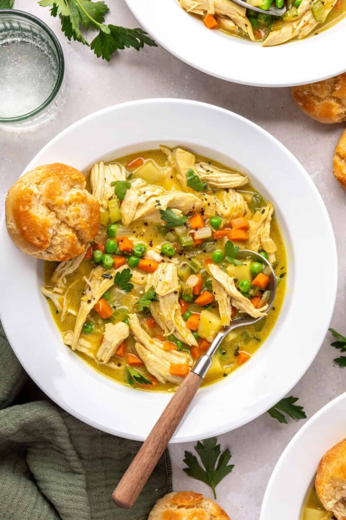 Bowl of chicken pot pie with veggies and shredded chicken, biscuit on the side, overhead shot.