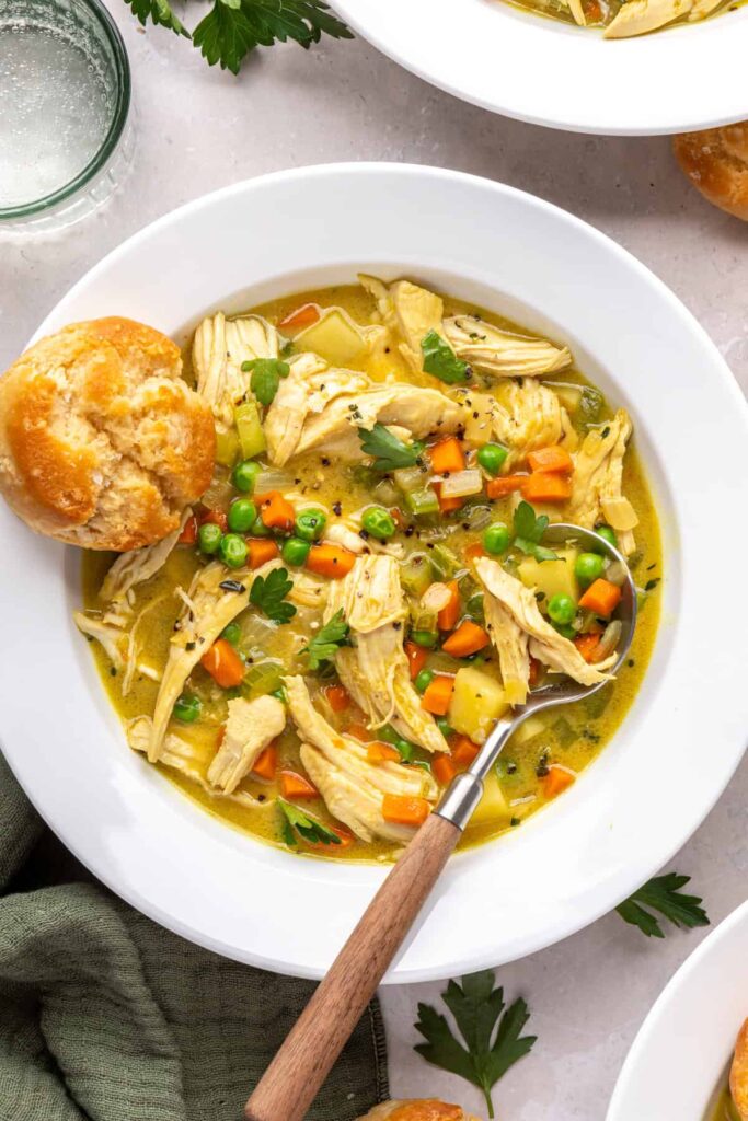 Bowl of chicken pot pie with veggies and shredded chicken, biscuit on the side, overhead shot.