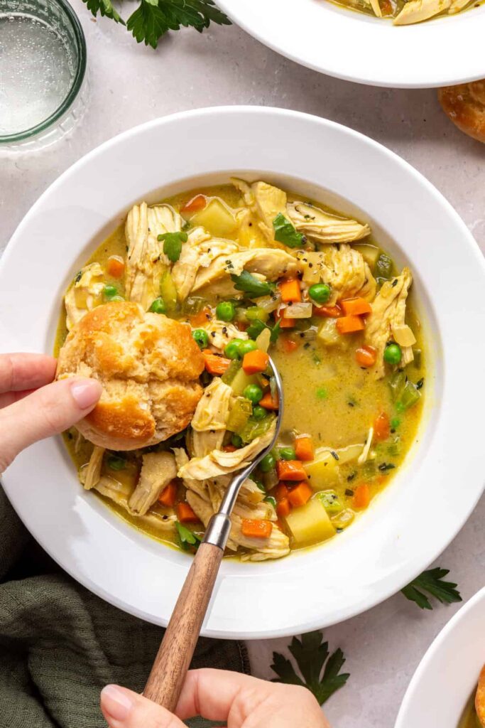 Overhead view of dipping a biscuit into one pot chicken pot pie served in a bowl with a spoon