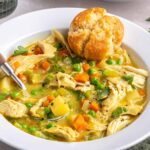 Angle shot of creamy chicken pot pie in a bowl with a spoon and warm biscuit.