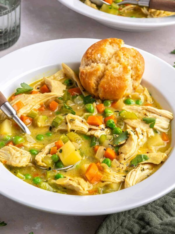 Angle shot of creamy chicken pot pie in a bowl with a spoon and warm biscuit.