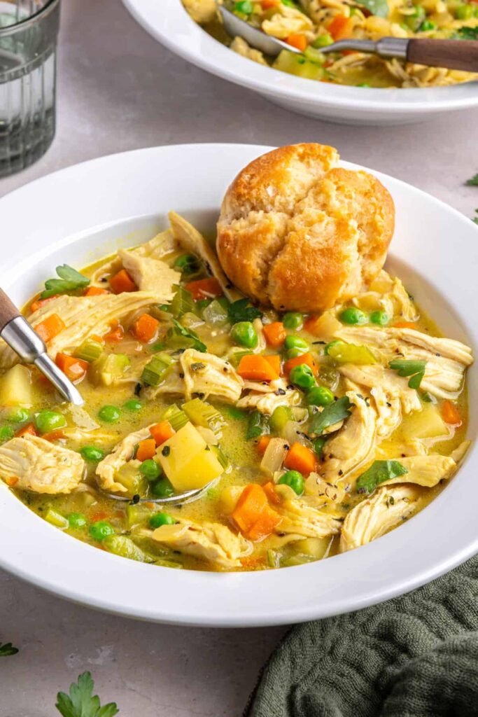 Angle shot of creamy chicken pot pie in a bowl with a spoon and warm biscuit.