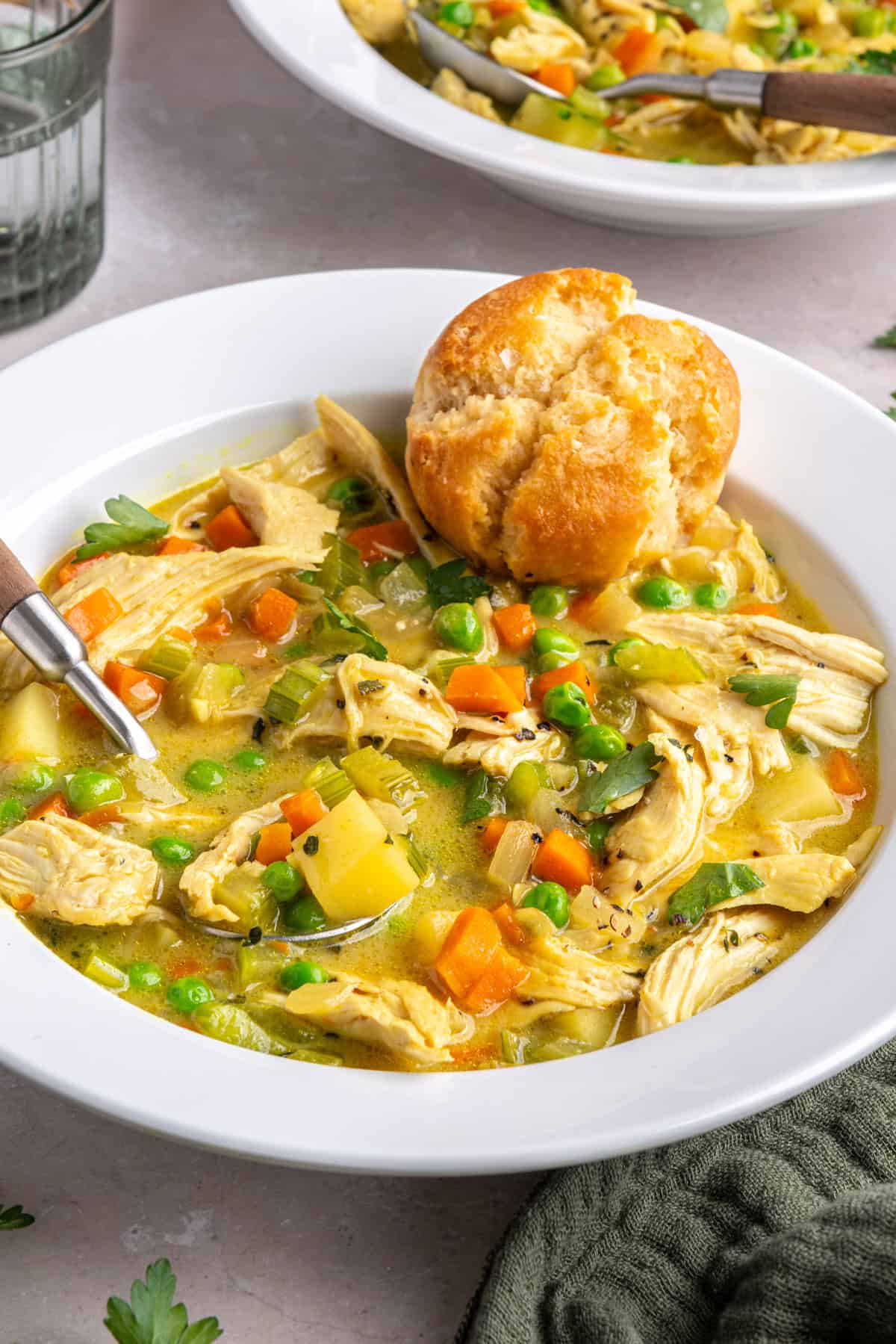 Angle shot of creamy chicken pot pie in a bowl with a spoon and warm biscuit.