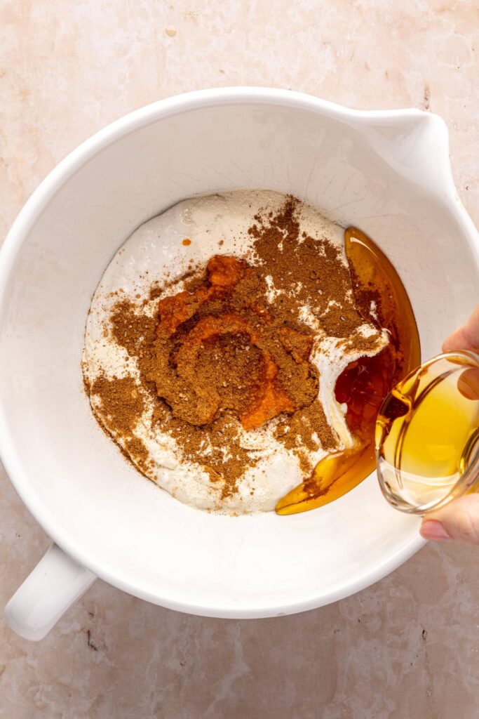 pouring maple syrup into a mixing bowl filled with ingredients to make homemade pumpkin cold foam