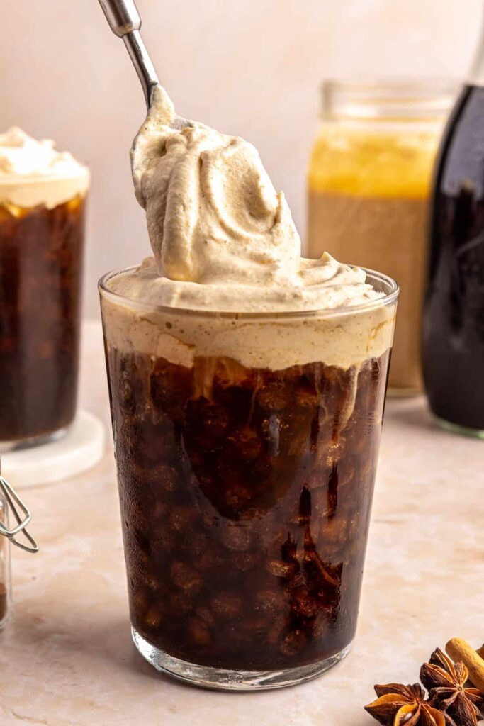 Dolloping pumpkin cold foam on top of a glass of iced coffee
