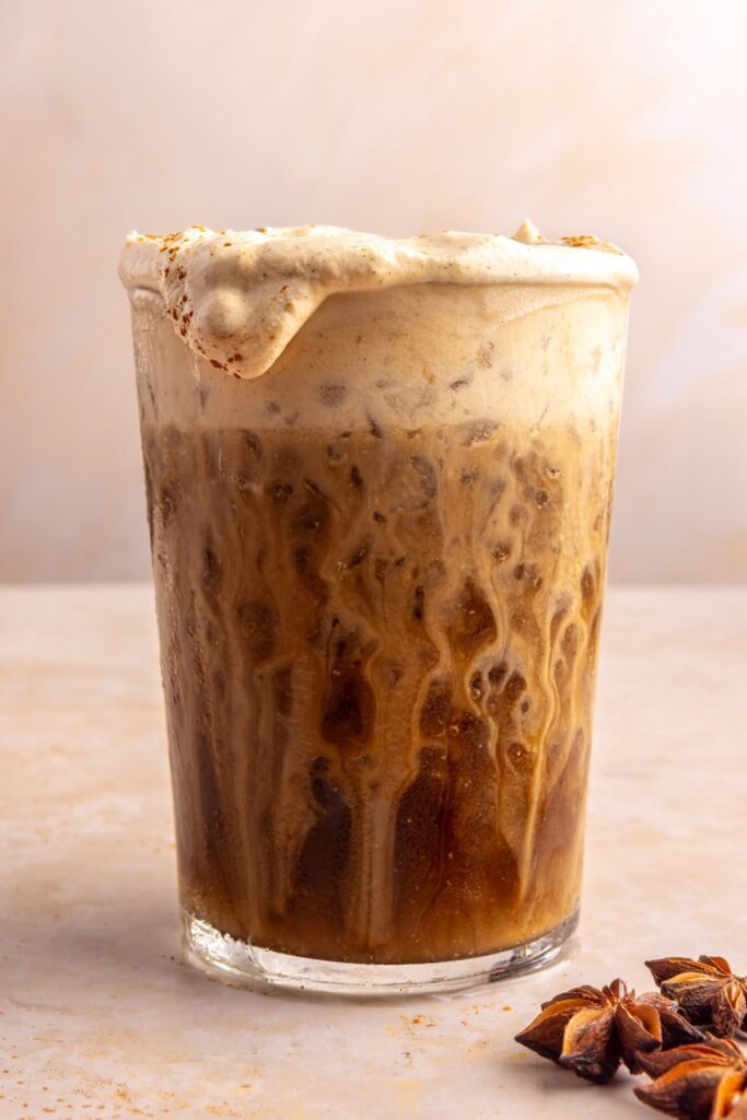 Layered pumpkin cold foam pouring over iced coffee edge