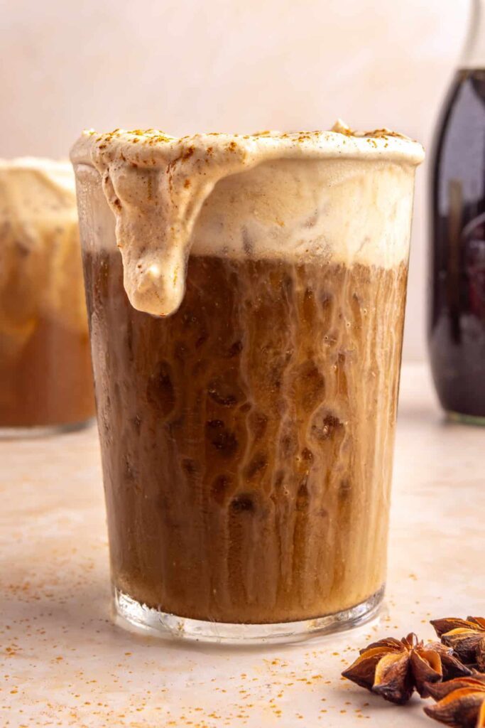 Layered pumpkin cold foam pouring over iced coffee edge