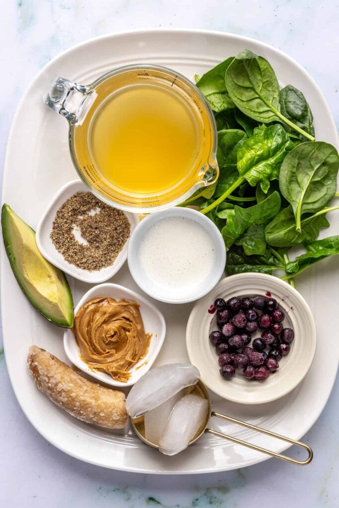 Overhead view of ingredients for a toddler smoothie: banana, avocado, spinach, peanut butter, blueberries, and milk