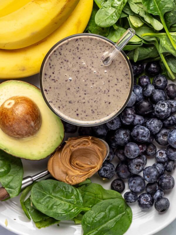 Overhead close-up of toddler smoothie in glass with banana, blueberries, spinach, peanut butter, and avocado arranged around it