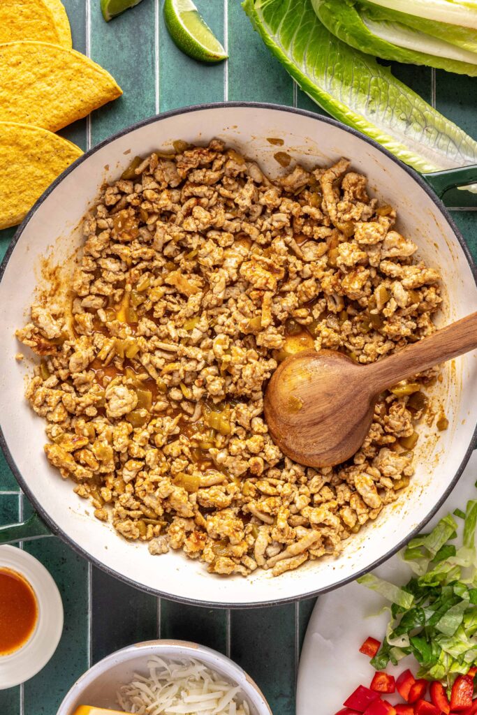 Stirring together the seasoned ground turkey with the taco seasoning, bone broth, and canned green chiles for turkey tacos
